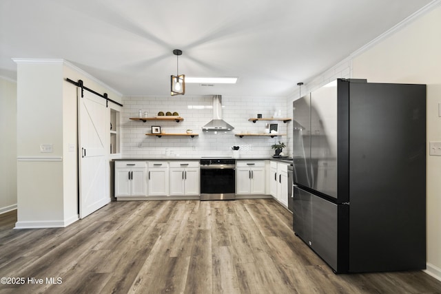 kitchen with pendant lighting, stainless steel fridge, range, a barn door, and wall chimney range hood