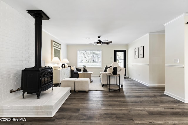 living room with crown molding, ceiling fan, dark hardwood / wood-style flooring, and a wood stove