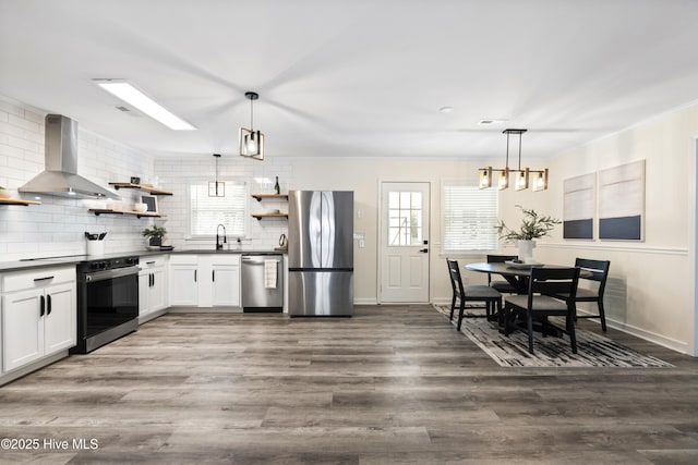 kitchen featuring wall chimney exhaust hood, sink, hanging light fixtures, stainless steel appliances, and white cabinets