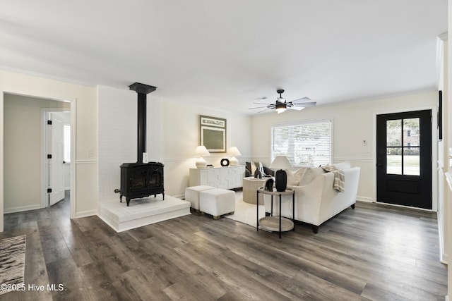 living room featuring ceiling fan, a wood stove, crown molding, and dark hardwood / wood-style floors