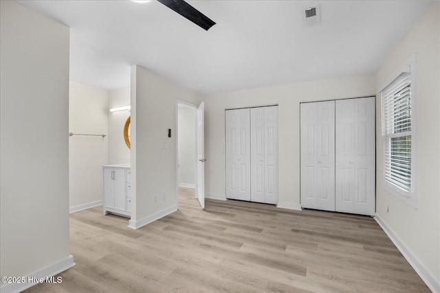 unfurnished bedroom featuring multiple closets, light hardwood / wood-style floors, and ceiling fan