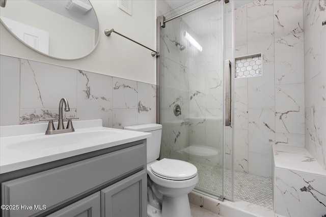 bathroom featuring vanity, toilet, a shower with door, and tile walls