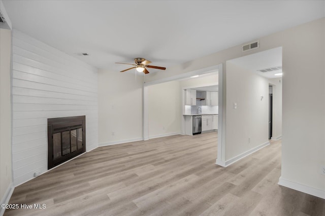 unfurnished living room featuring ceiling fan, a large fireplace, sink, and light wood-type flooring