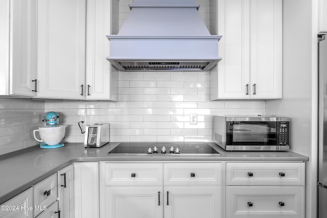 kitchen featuring decorative backsplash, white cabinetry, black electric stovetop, and custom exhaust hood