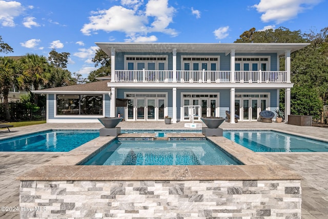 back of property with a pool with hot tub, a balcony, a patio, and french doors