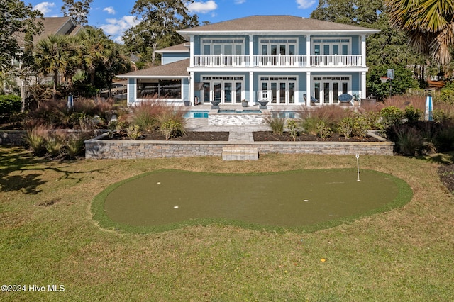 rear view of house with a lawn, a balcony, and french doors