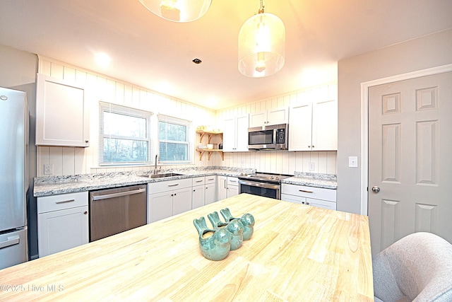 kitchen featuring butcher block countertops, white cabinetry, sink, hanging light fixtures, and stainless steel appliances