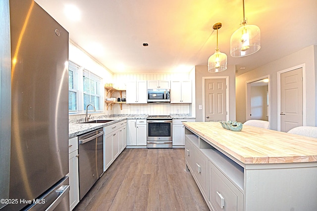 kitchen with appliances with stainless steel finishes, sink, white cabinets, and decorative light fixtures