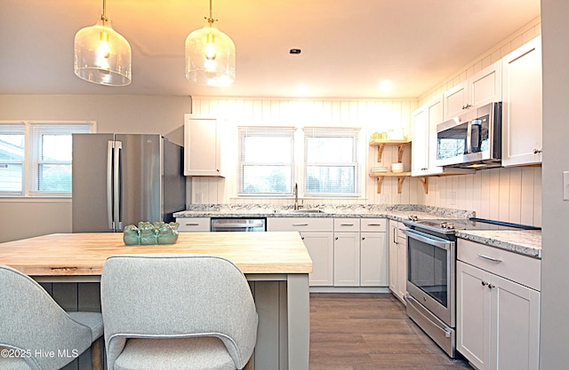 kitchen with butcher block counters, sink, decorative light fixtures, stainless steel appliances, and white cabinets