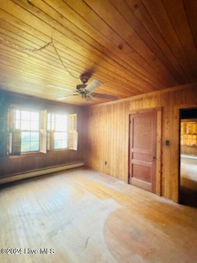 empty room with a baseboard radiator, ceiling fan, wooden ceiling, and wood walls