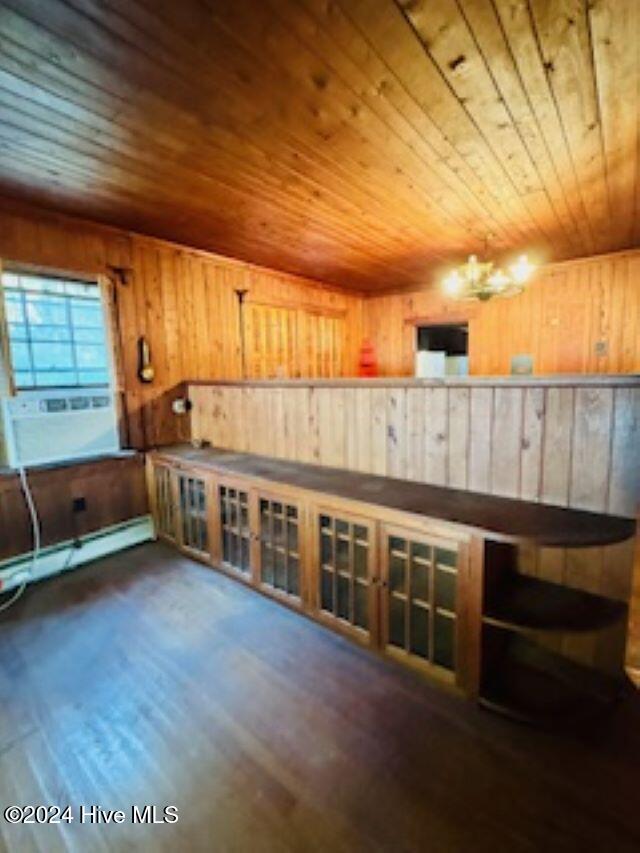 interior space with dark hardwood / wood-style flooring, wood ceiling, baseboard heating, a chandelier, and wood walls