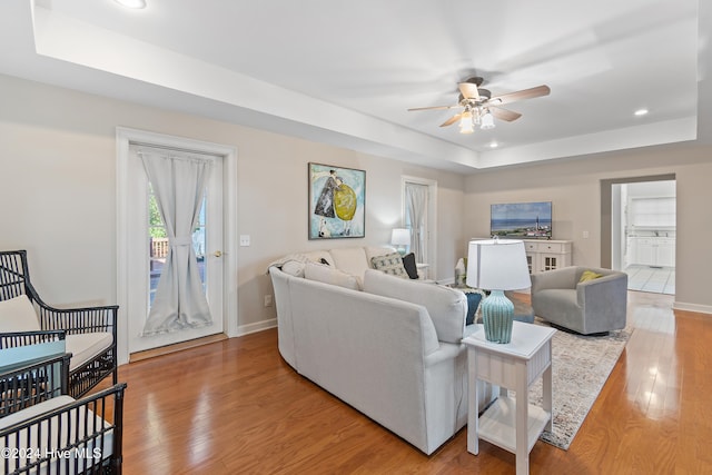 living room featuring ceiling fan, light hardwood / wood-style floors, and a tray ceiling