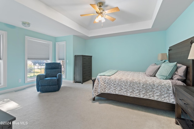 bedroom featuring light colored carpet, a raised ceiling, and ceiling fan