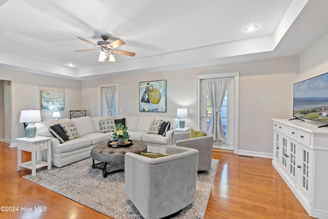 living room with ceiling fan, a raised ceiling, and light wood-type flooring