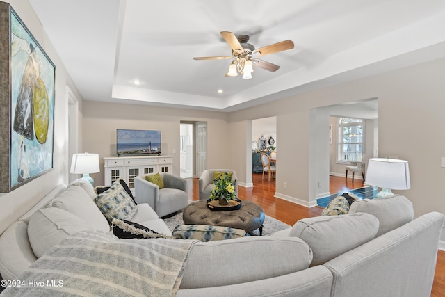 living room featuring ceiling fan, light wood-type flooring, and a tray ceiling