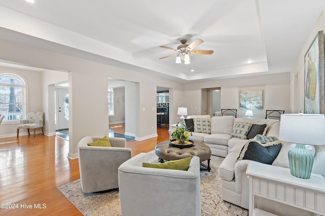 living room featuring light wood-type flooring, a raised ceiling, and ceiling fan