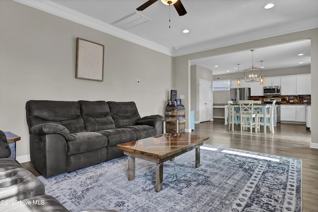 living room with ceiling fan with notable chandelier, crown molding, and dark wood-type flooring