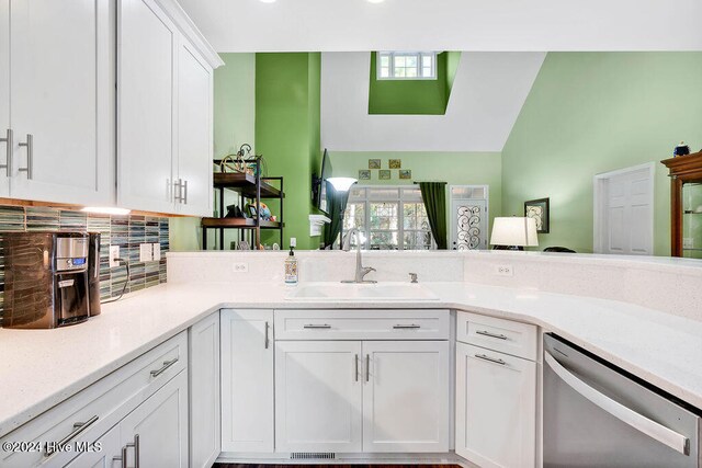 kitchen featuring backsplash, stainless steel dishwasher, sink, white cabinetry, and lofted ceiling