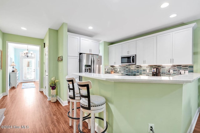 kitchen with decorative backsplash, light wood-type flooring, stainless steel appliances, an inviting chandelier, and white cabinets