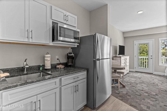 kitchen featuring white cabinets, sink, dark stone countertops, appliances with stainless steel finishes, and light hardwood / wood-style floors