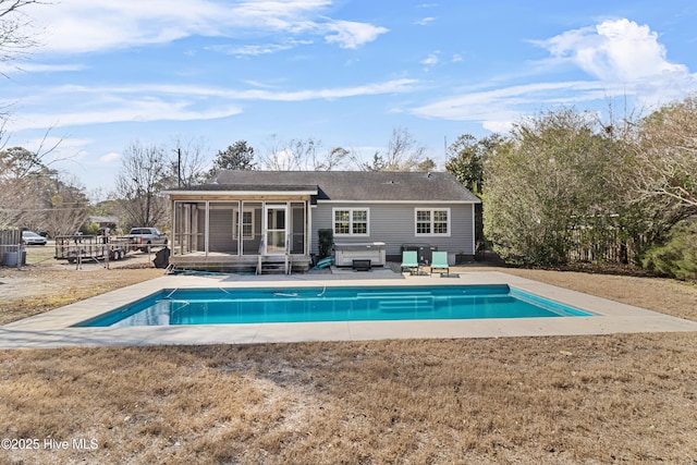 rear view of house with a swimming pool with hot tub, a patio area, a sunroom, and a lawn