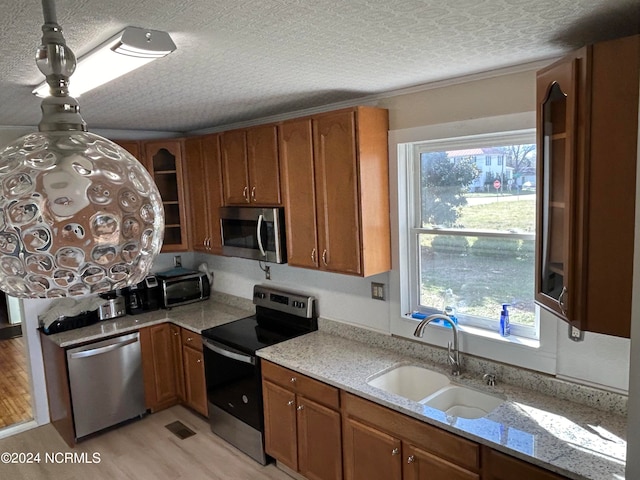 kitchen with appliances with stainless steel finishes, light hardwood / wood-style floors, light stone counters, and a healthy amount of sunlight