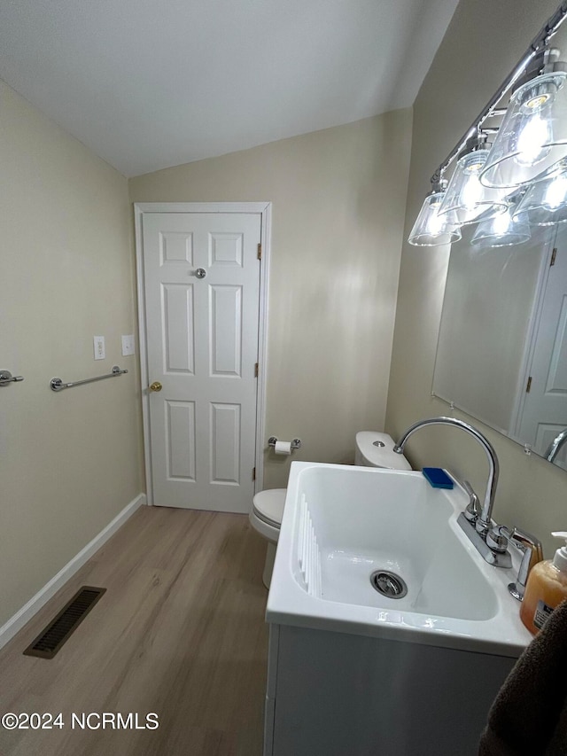 bathroom with toilet, hardwood / wood-style floors, lofted ceiling, and sink