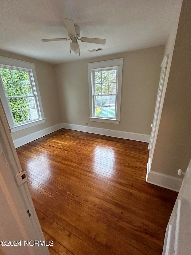 unfurnished room featuring ceiling fan, a healthy amount of sunlight, and dark wood-type flooring