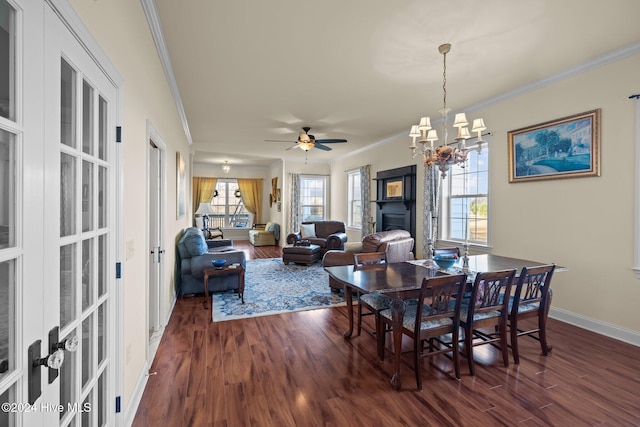 dining area featuring ceiling fan with notable chandelier, dark hardwood / wood-style floors, a stone fireplace, and crown molding