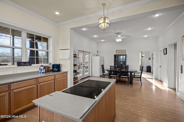 kitchen featuring a center island, black electric stovetop, ceiling fan with notable chandelier, hanging light fixtures, and a wealth of natural light