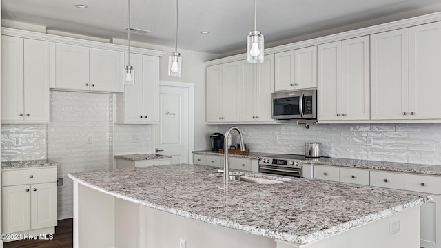 kitchen featuring appliances with stainless steel finishes, a center island with sink, white cabinetry, and hanging light fixtures