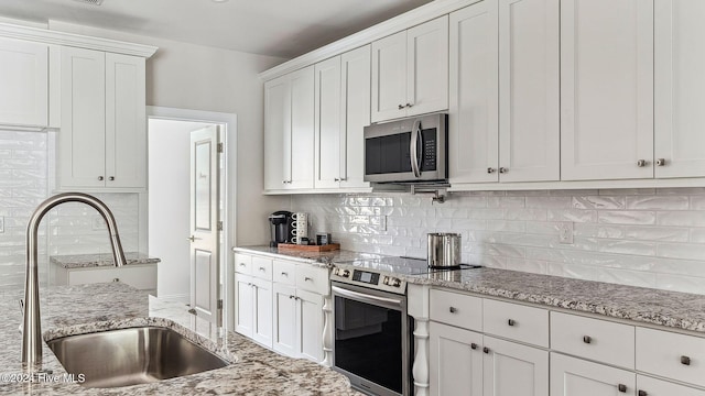 kitchen with backsplash, sink, light stone countertops, appliances with stainless steel finishes, and white cabinetry