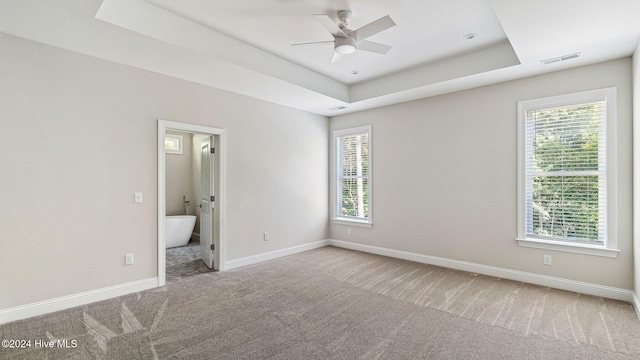 unfurnished bedroom featuring carpet flooring, a tray ceiling, ensuite bath, and ceiling fan