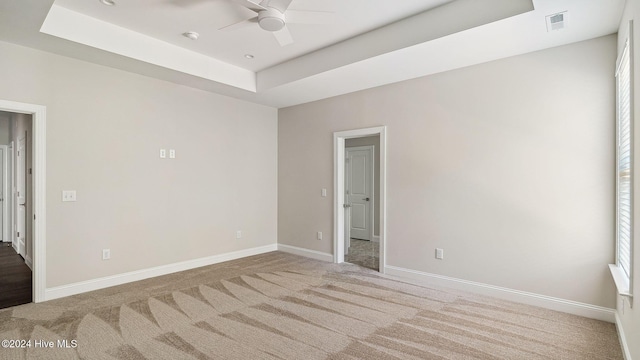 carpeted spare room with a raised ceiling and ceiling fan