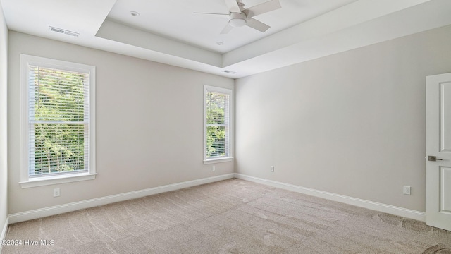 carpeted empty room with plenty of natural light, ceiling fan, and a raised ceiling