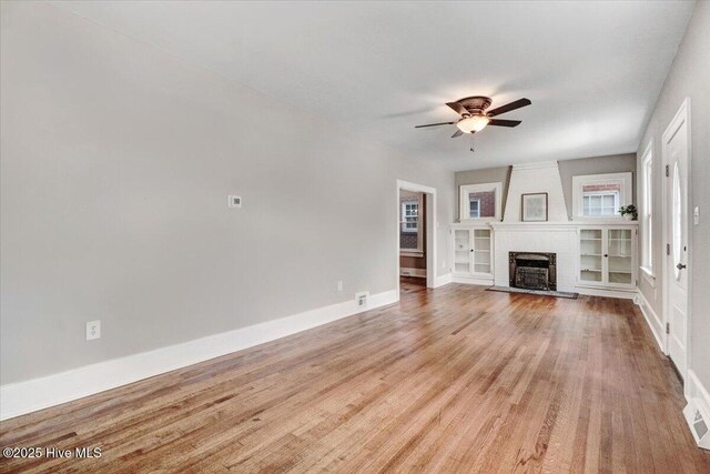 unfurnished living room featuring baseboards, a ceiling fan, a brick fireplace, and wood finished floors