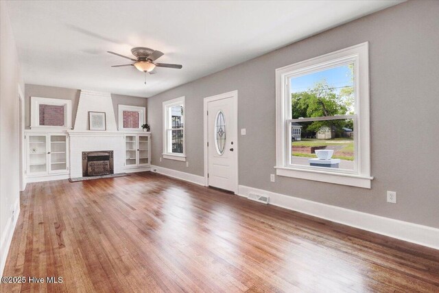 unfurnished living room with a wealth of natural light, a ceiling fan, wood finished floors, and visible vents