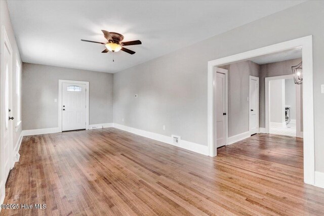 spare room featuring baseboards, visible vents, light wood finished floors, and ceiling fan with notable chandelier