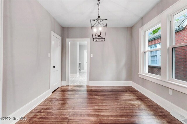 unfurnished dining area with an inviting chandelier, baseboards, dark wood finished floors, and visible vents