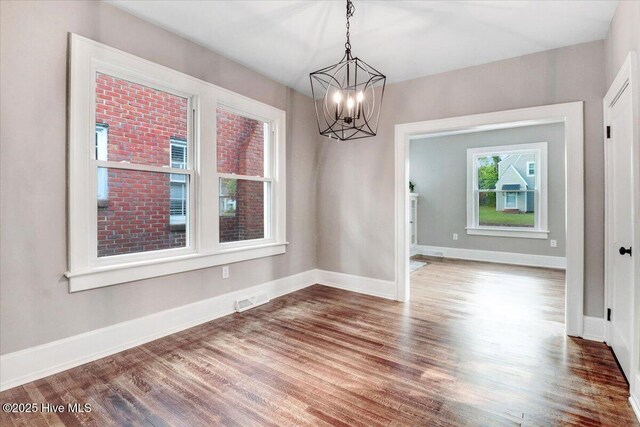 unfurnished dining area featuring baseboards, wood finished floors, and a chandelier