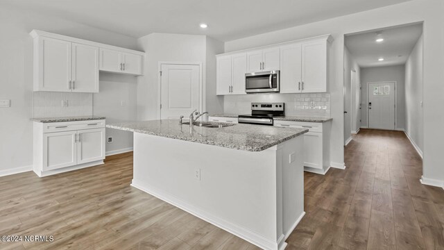 kitchen featuring white cabinets, appliances with stainless steel finishes, a center island with sink, and light hardwood / wood-style floors