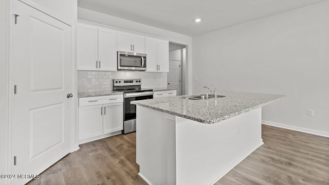 kitchen with appliances with stainless steel finishes, sink, light hardwood / wood-style flooring, white cabinets, and an island with sink