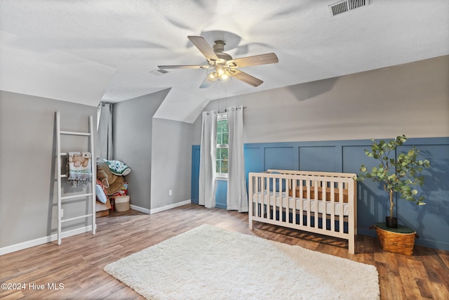 bedroom featuring a textured ceiling, ceiling fan, a crib, and hardwood / wood-style flooring