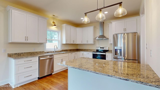 kitchen featuring white cabinets, sink, hanging light fixtures, wall chimney exhaust hood, and appliances with stainless steel finishes