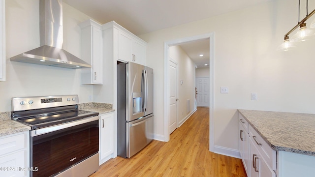 kitchen with light stone countertops, white cabinetry, stainless steel appliances, wall chimney range hood, and light hardwood / wood-style flooring