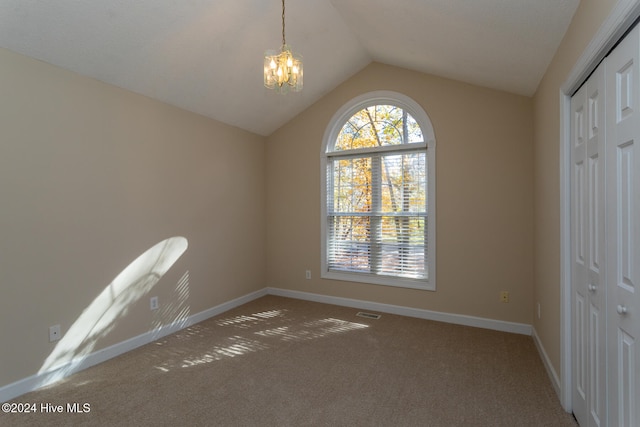 empty room featuring carpet, lofted ceiling, and an inviting chandelier