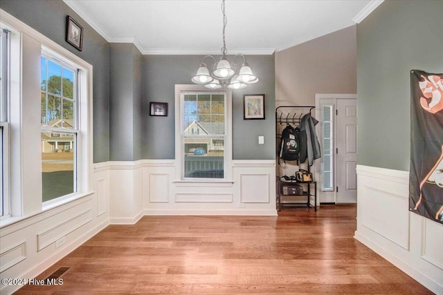 unfurnished dining area featuring crown molding, wood-type flooring, and a notable chandelier