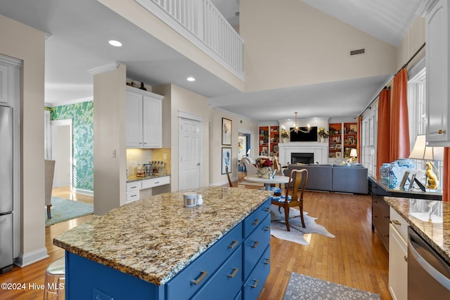 kitchen with light stone countertops, blue cabinets, light hardwood / wood-style flooring, white cabinets, and a center island