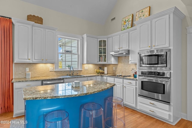 kitchen featuring a center island, white cabinets, vaulted ceiling, light wood-type flooring, and stainless steel appliances