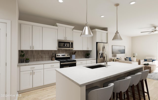 kitchen with appliances with stainless steel finishes, sink, a center island with sink, white cabinets, and hanging light fixtures